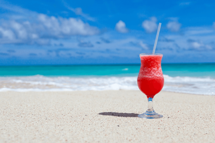 Primer plano de una bebida exótica roja sobre una playa caribeña. Mar turquesa sobre cielo azul. 