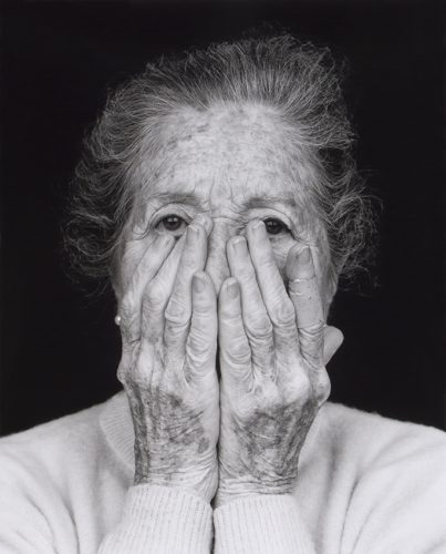 Foto en blanco y negro de una mujer mayor tapándose la cara con las dos manos