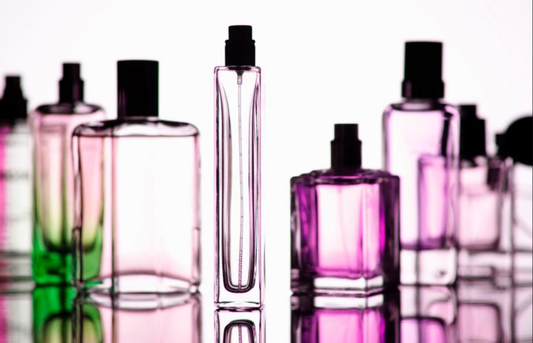 Foto con varios frascos de perfumes vacíos que están dispuestos de forma artística. Botes translúcidos sobre un fondo blanco.