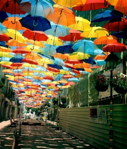 Imagen de una calle con adornos de paraguas de muchos colores en la parte superior a modo de techo.