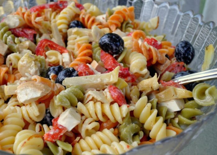 En la foto un zoom al detalle de una ensalada de pasta compuesta por espirales, pimiento rojo, dados de queso fresco y olivas