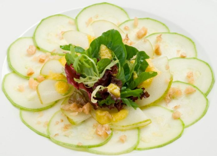 En la foto un carpaccio de verduras con pepino cortado muy fino y hojas de ensalada además de gajos de limón