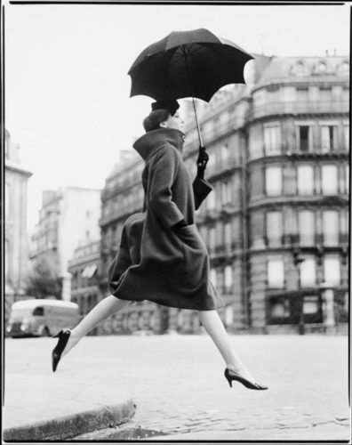 Foto artística de una mujer dando un salto y con un paraguas abierto en una mano.