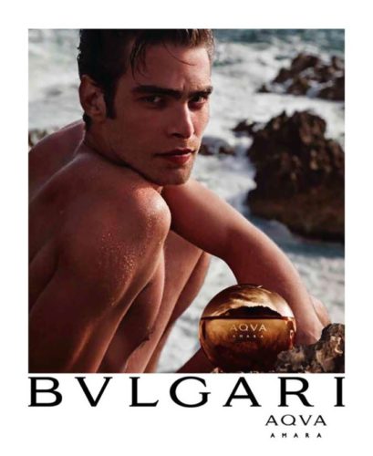 Foto de un modelo en la playa anunciando el perfume de la marca Bvlgari