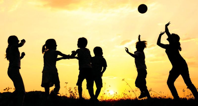 Foto a contraluz donde se ve la silueta de varios niños jugando con una pelota