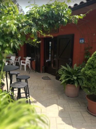 En la foto aparece la entrada del restaurant con muchas plantas y unas sillas en una de sus terrazas