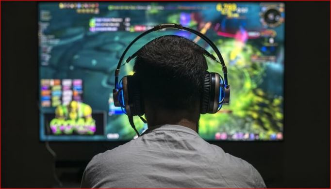 Una foto donde se ve a un gamer de espaldas con auriculares frente a una pantalla con un juego del tipo MMO