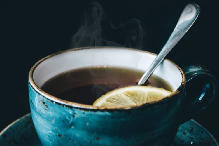 En la foto una infusión de té con una rodaja de limón servida en una bonita taza azulada con el interior blanco y el canto dorado