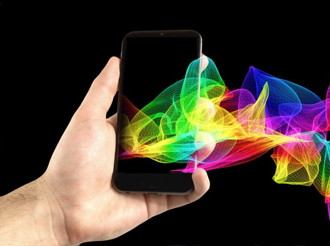 Una composición digital donde se ve una mano con un teléfono móvil del que salen unas gráficas en forma de malla tridimensional con los colores del arcoiris