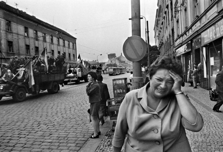 Foto en blanco y negro. Mujer llorando mientras hay camiones con soldados en las calles