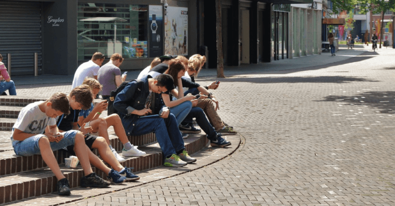 Grupo de adolescentes sentados en una plaza pública todos con el móvil