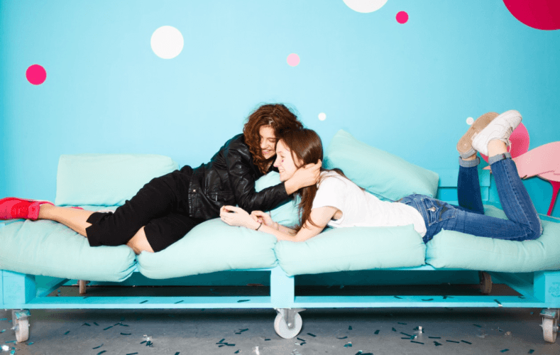 Dos chicas abrazadas de forma amistosa sobre una cama en una habitación juvenil pintada de azul
