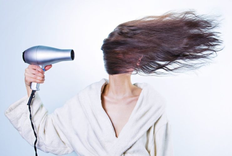 En la foto una mujer con un potente secador de mano secando un frondoso cabello que le tapa incluso la caro