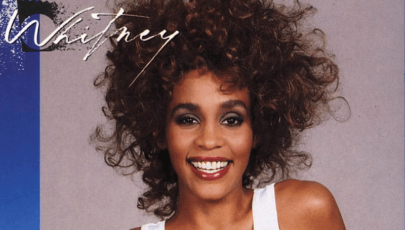 En la foto, la portada de un disco con una joven y sonriente Whitney Houston con una camiseta de tirantes blanco y el pelo alborotado