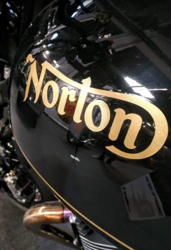 El logotipo de Norton en color dorado sobre una Norton Comando en color negro