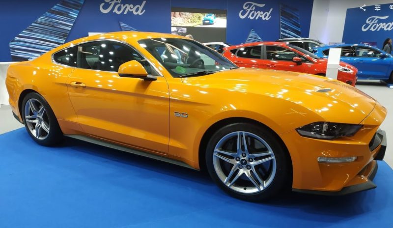 En la foto un Ford Mustang en color naranja visto desde el lateral