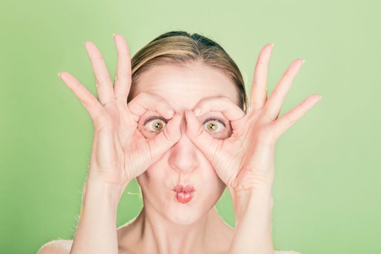 En la foto una imagen divertida de una chica con los ojos claros con sus manos haciendo las veces de gafas
