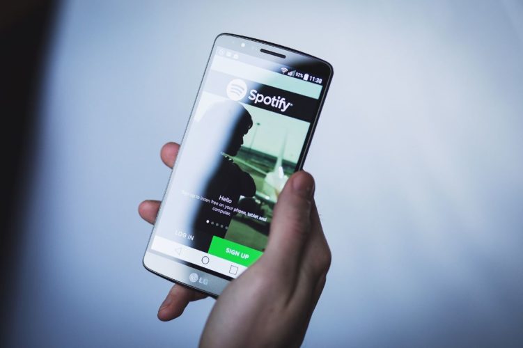 En la foto se ve una mano sosteniendo un móvil de la marca LG en alto con la app de Spotify abierta