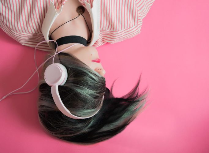 Una foto de una chica que está boca abajo escuchando música con sus auriculares