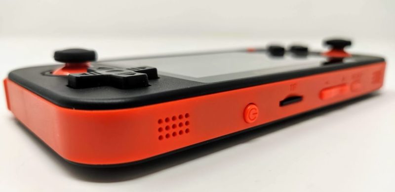 La consola RG350 fotografiada para que se vea su lateral inferior, con los altavoces y la entrada de la tarjeta microSD