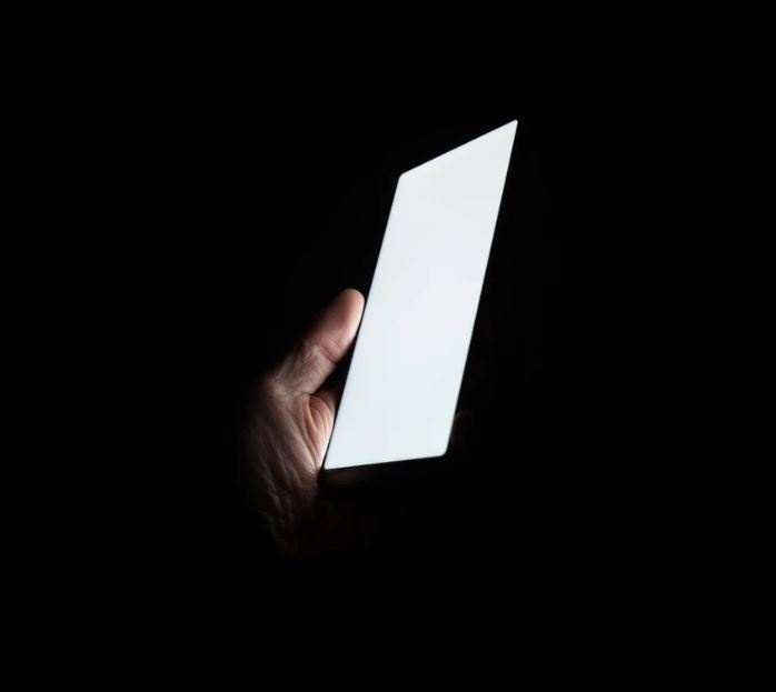 Foto de una pantalla de móvil suspendida por una mano con un fondo totalmente obscuro